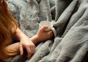 overhead view of woman's hands holding mug over grey fuzzy blanket