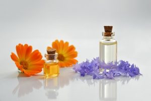 two small glass bottles with corks, orange flowers and purple flowers