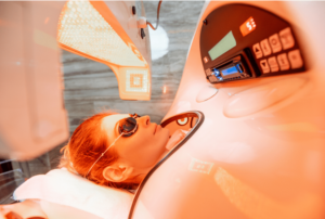 Woman lying in a red light therapy capsule with her head out.